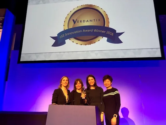 Four women stand onstage holding an award, with a screen reading “Verdantix HSE Innovation Award Winner 2018,” celebrating the Cority Client’s achievement.