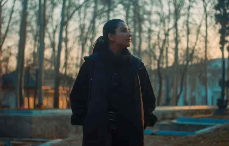 Woman in a dark coat stands outdoors at sunset, with bare trees and soft sunlight in the background, reminiscent of the calm after a rigorous FDA Inspection.