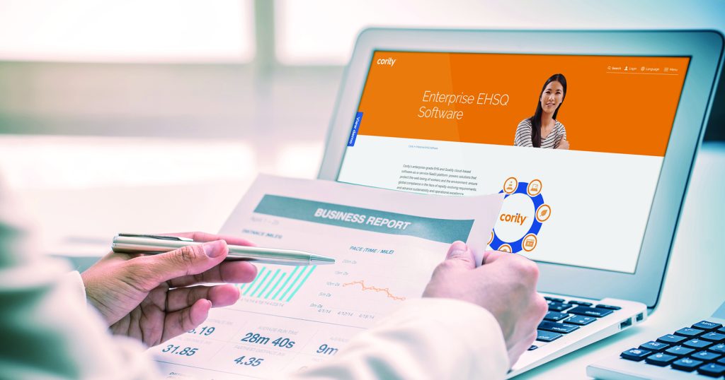 A person reviews a business report beside a laptop displaying Cority’s enterprise EHSQ software website, evaluating its occupational hygiene features for the Australian market.