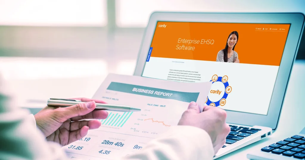 A person reviews a business report beside a laptop displaying Cority’s enterprise EHSQ software website, evaluating its occupational hygiene features for the Australian market.
