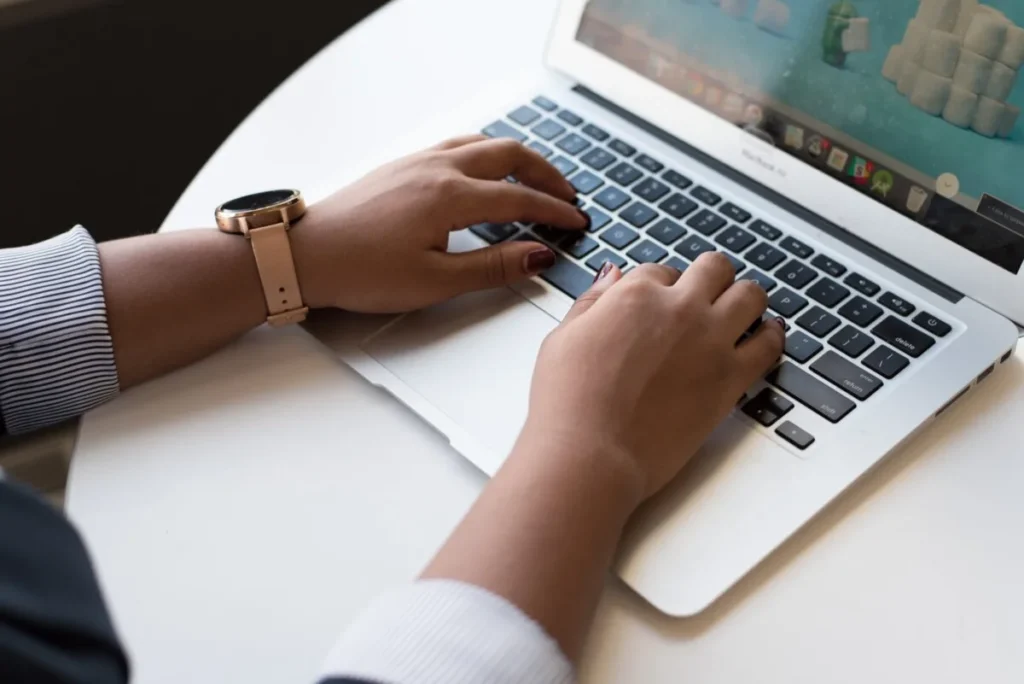 Person typing on a laptop at a white table, wearing a watch and striped shirt sleeves—highlighting potential ergonomic risk factors in everyday work settings.
