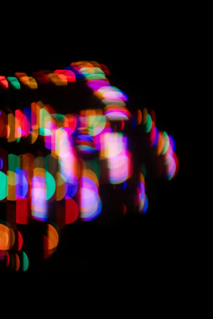 Abstract image of colorful, out-of-focus lights forms soft, circular shapes against a black background, evoking a vibrant bokeh effect—an artful reminder to consider our carbon footprint amid the beauty of red, blue, green, yellow, and pink hues.