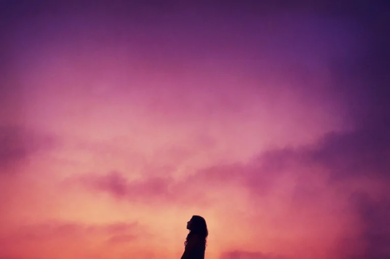 Silhouette of a person standing against a colorful sky at sunset, featuring purple and orange hues, capturing the spirit of EHS & Sustainability in harmony with nature’s beauty.