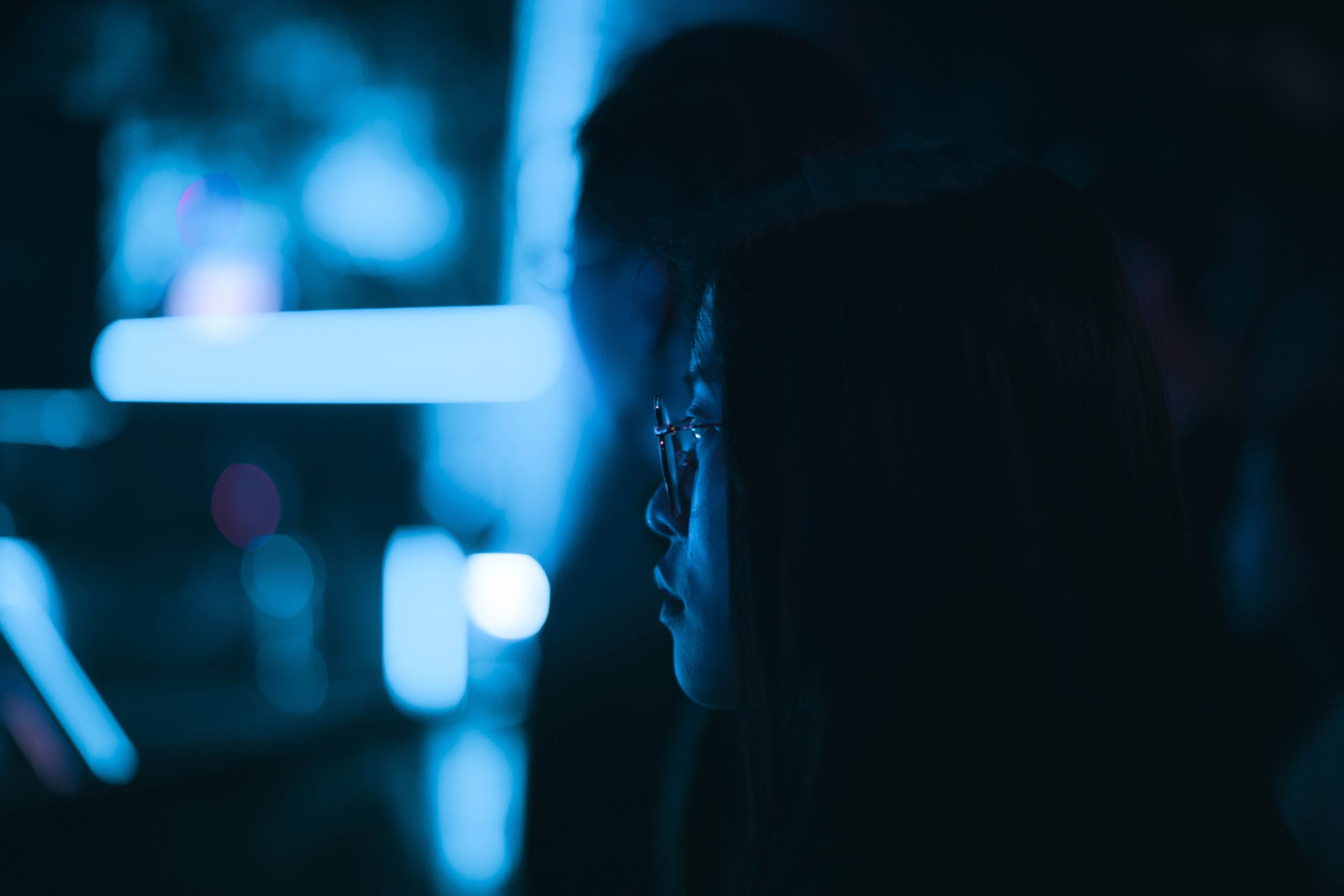 A person in glasses sits in a dark room, illuminated by blue light, with blurred shapes in the background—capturing the modern vibe of a True SaaS EHS workspace.