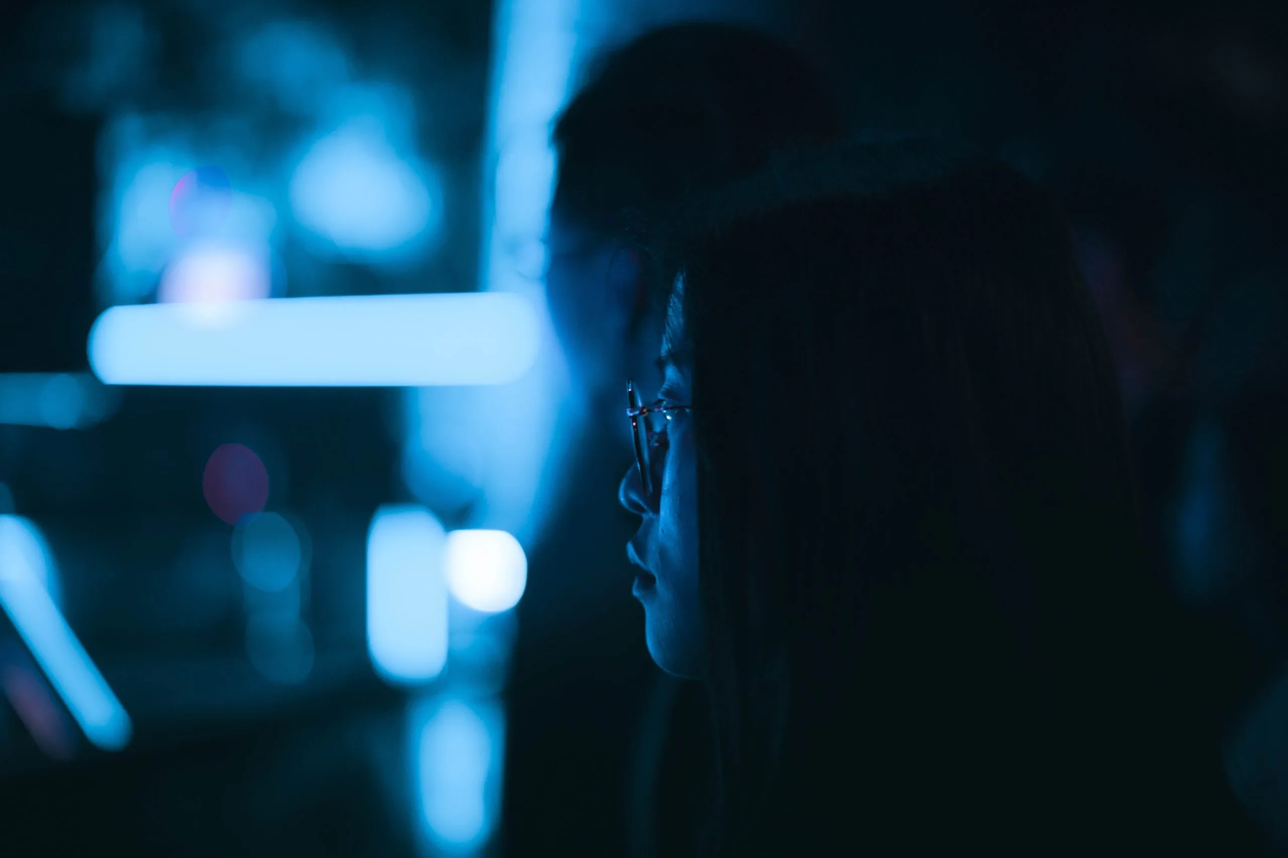 A person in glasses sits in a dark room, illuminated by blue light, with blurred shapes in the background—capturing the modern vibe of a True SaaS EHS workspace.