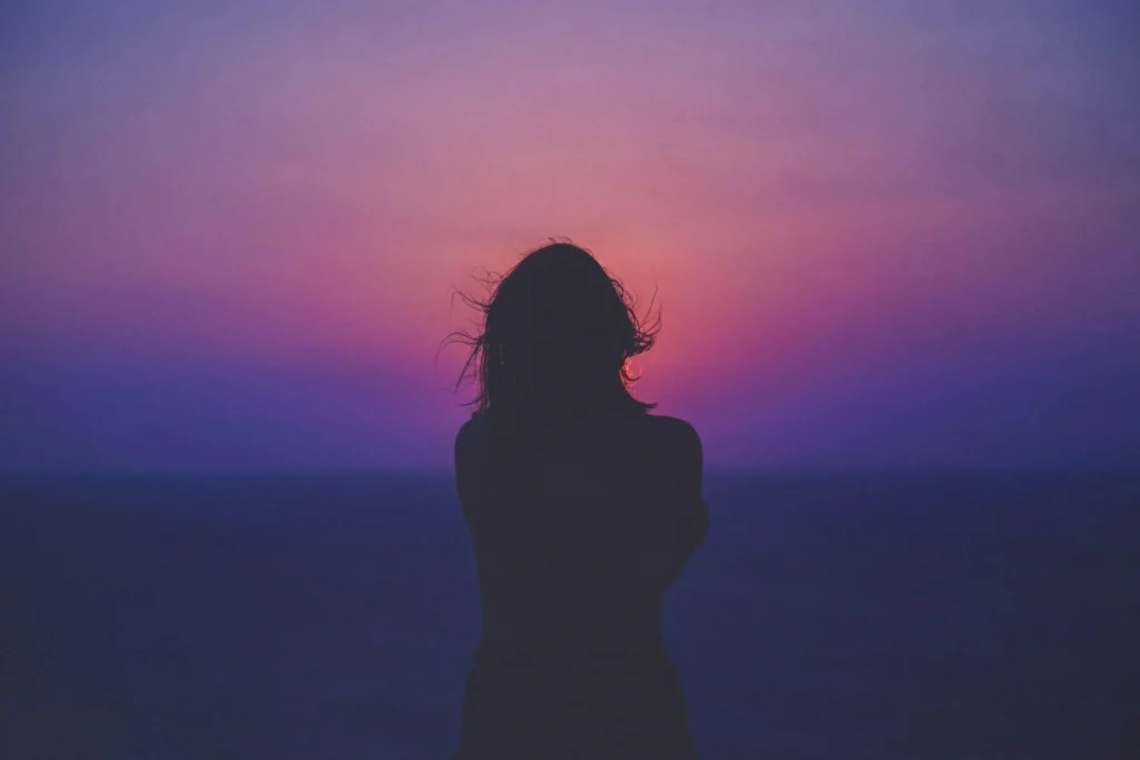 Silhouette of a person standing by the sea at sunset with a colorful pink and purple sky, reflecting on the importance of sustainability reporting.