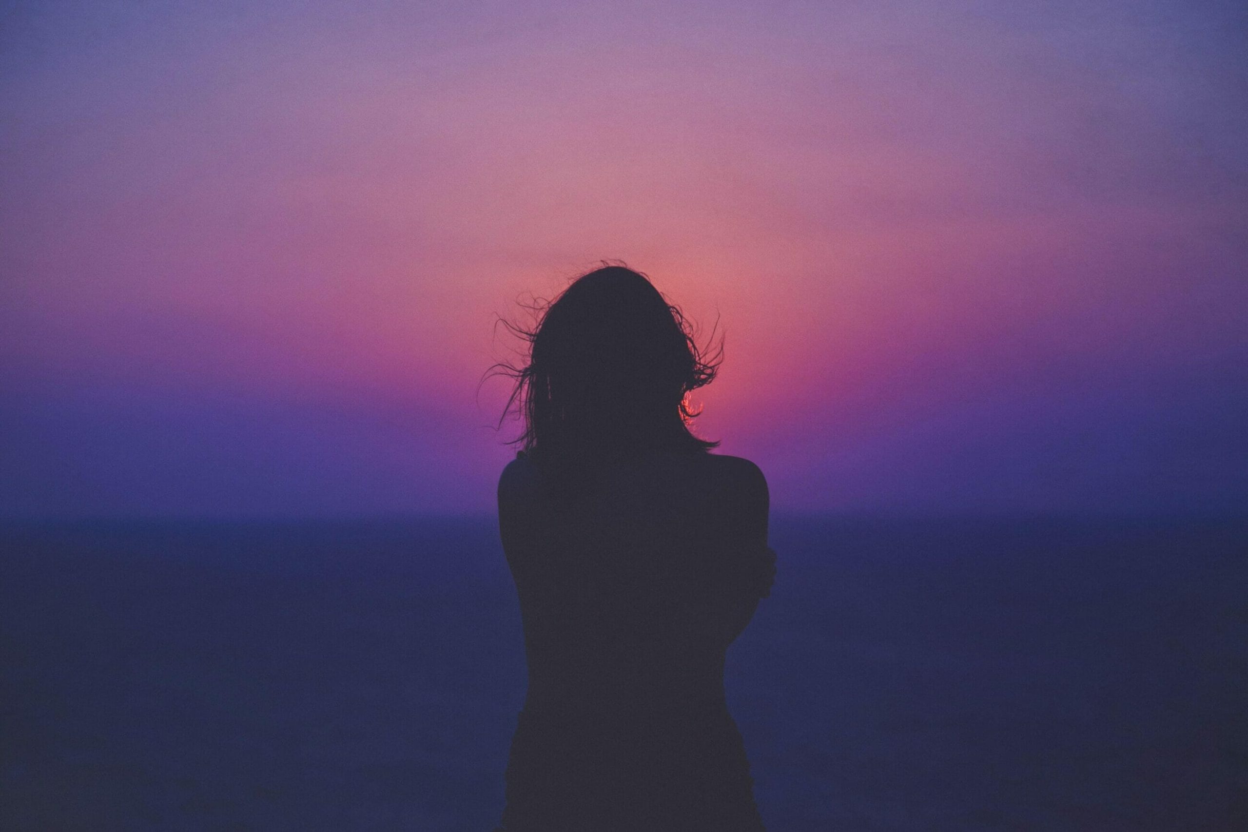 Silhouette of a person standing by the sea at sunset with a colorful pink and purple sky, reflecting on the importance of sustainability reporting.