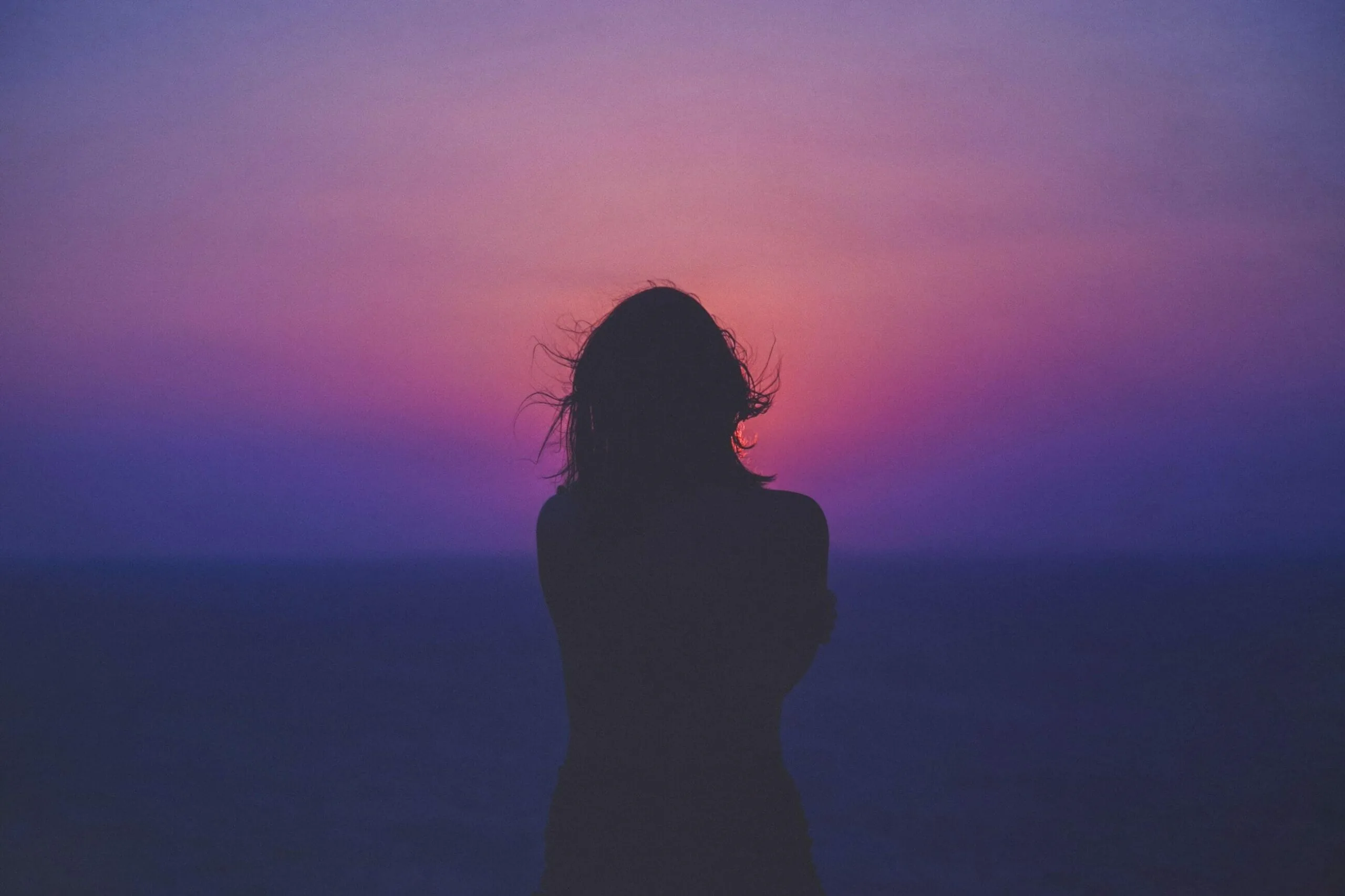 Silhouette of a person standing by the sea at sunset with a colorful pink and purple sky, reflecting on the importance of sustainability reporting.