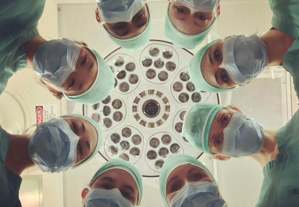 Six surgeons in scrubs and masks look down under a bright surgical light in an operating room, embodying the commitment to ESG in Healthcare through responsible and ethical medical practices.