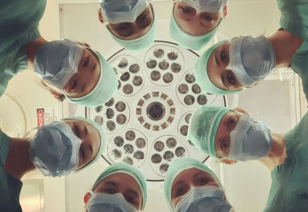 Six surgeons in scrubs and masks look down under a bright surgical light in an operating room, embodying the commitment to ESG in Healthcare through responsible and ethical medical practices.