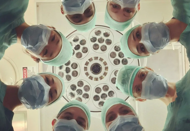 Six surgeons in scrubs and masks look down under a bright surgical light in an operating room, embodying the commitment to ESG in Healthcare through responsible and ethical medical practices.