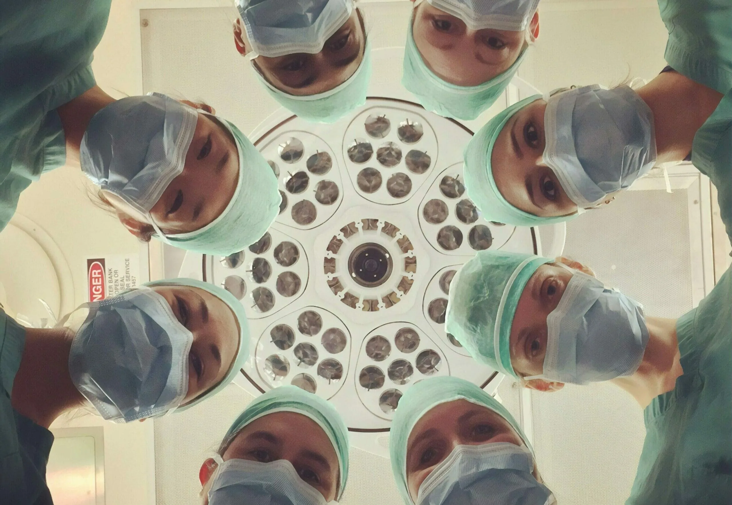 Six surgeons in scrubs and masks look down under a bright surgical light in an operating room, embodying the commitment to ESG in Healthcare through responsible and ethical medical practices.
