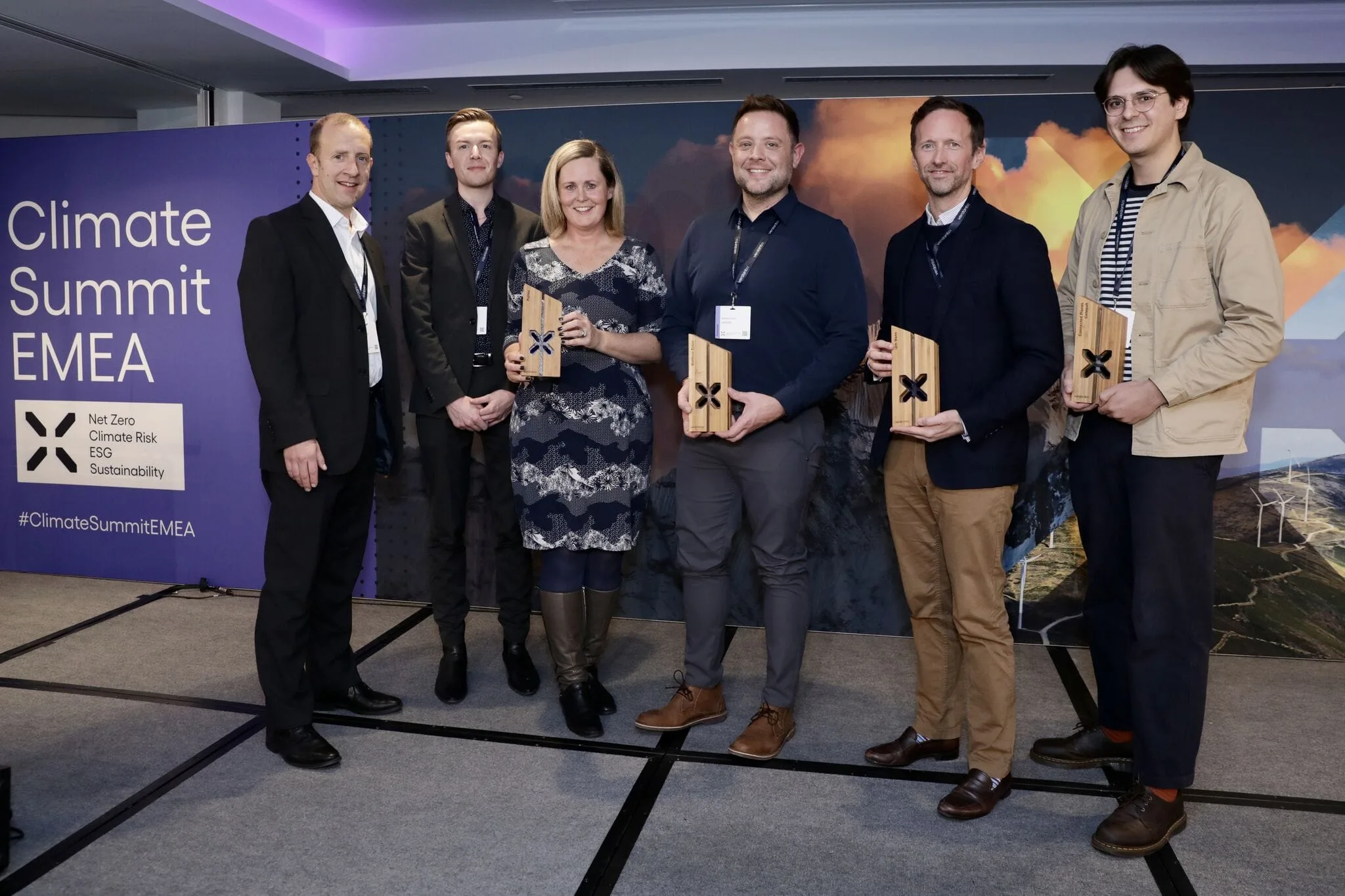 Six people holding awards, including the Cority Fujitsu Award, stand on stage at the Climate Summit EMEA with a banner and scenic backdrop.