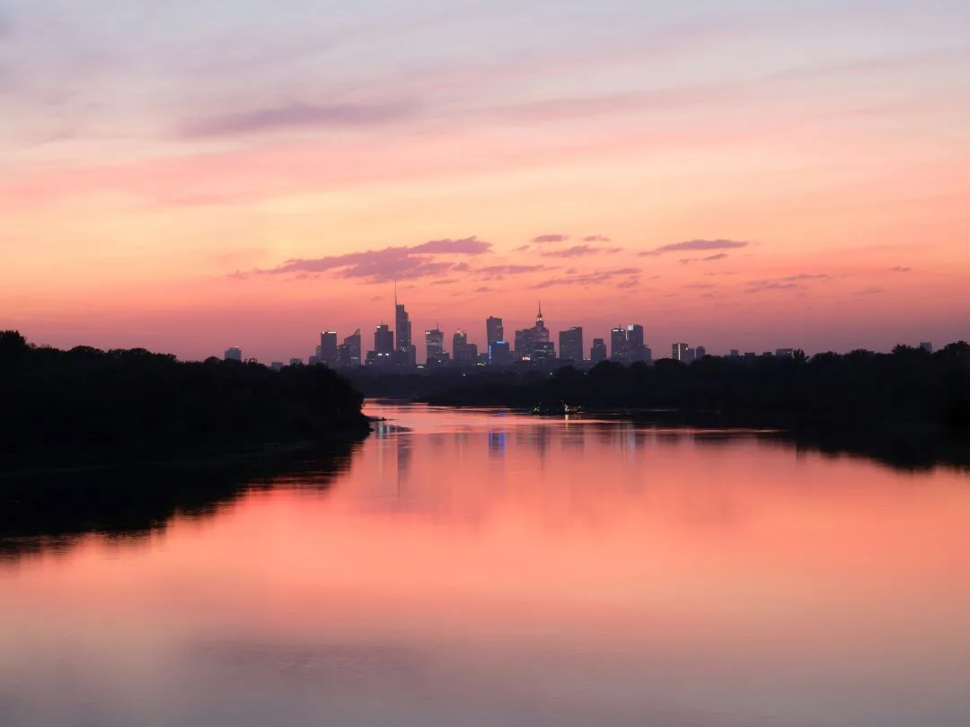 City skyline at sunset reflected on a calm river, with pink and purple hues in the sky and water—an inspiring scene reminiscent of innovative Software CSRD solutions shaping our urban future.