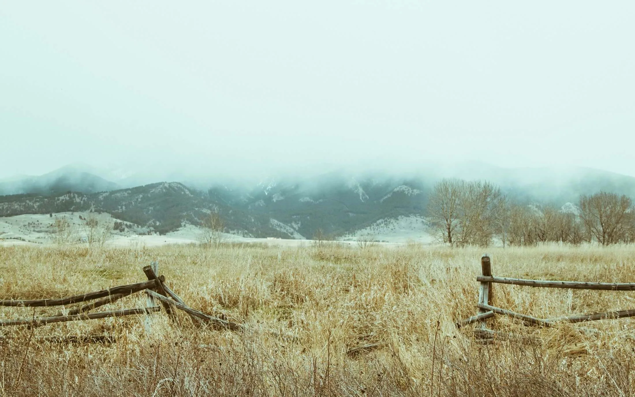 Broken wooden fence in a dry field with foggy mountains and bare trees in the background, illustrating the key benefits of circular economy practices for EHS professionals striving to restore and preserve natural landscapes.