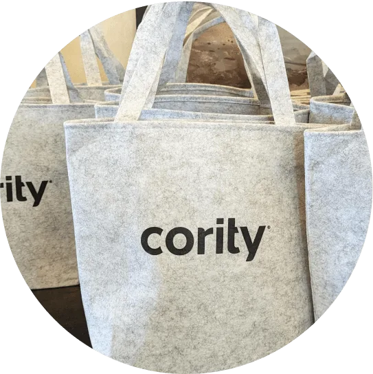 A close-up of several light gray felt tote bags, with "cority" printed in black on the front, standing upright and overlapping—highlighting Sustainability at Cority through eco-friendly design.