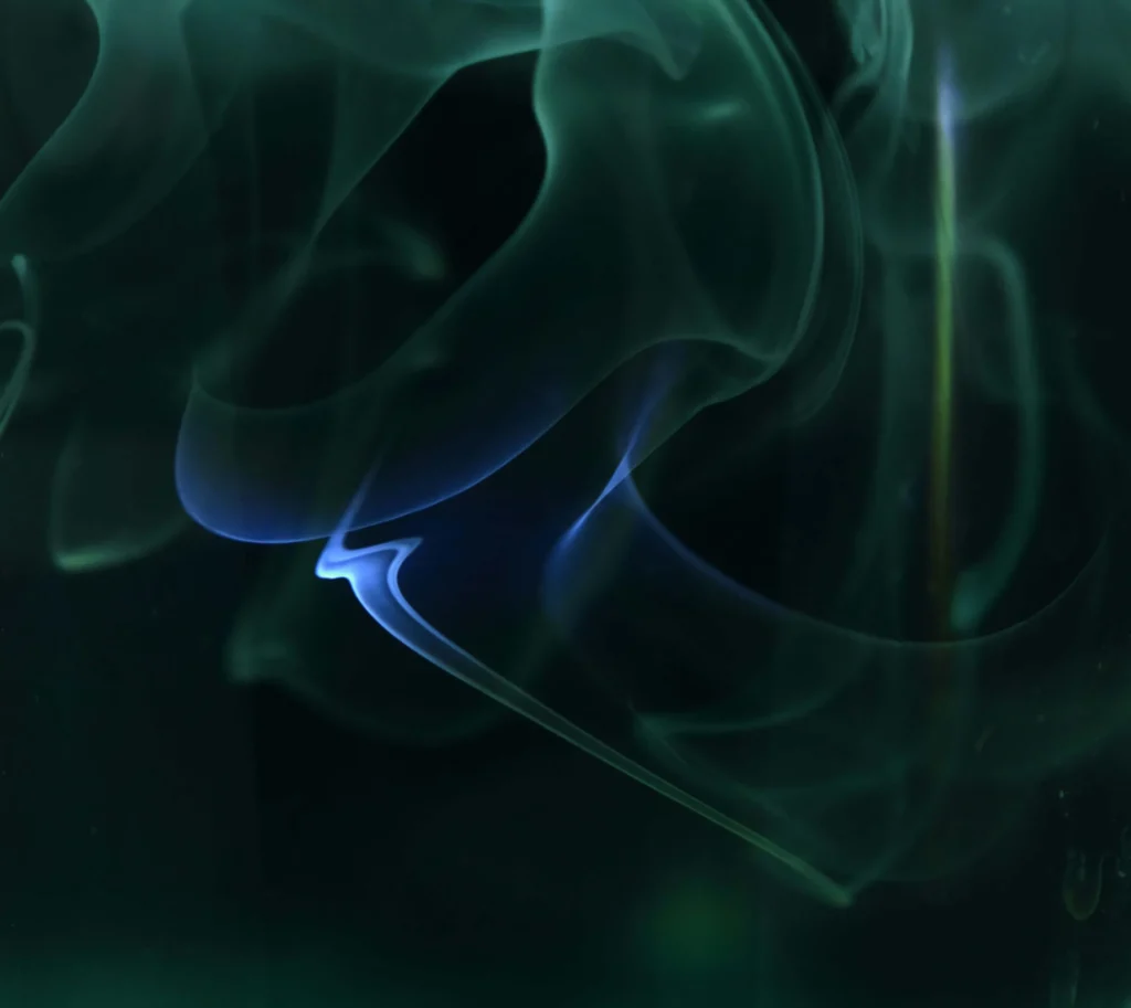 Wisps of blue and green smoke swirl abstractly against a dark background, evoking the dynamic flow of user experience in multilingual UX design.