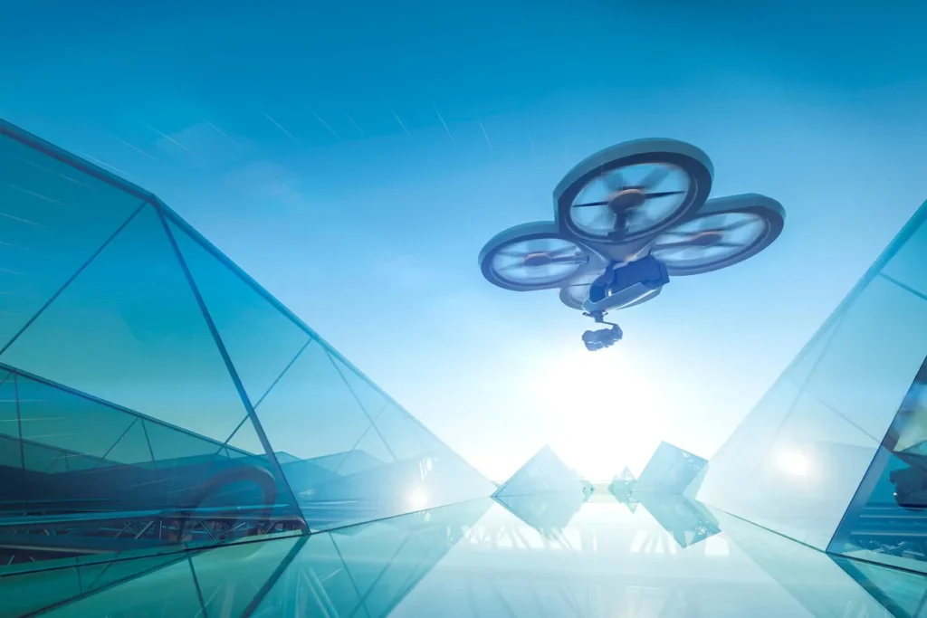 A camera drone with three propellers flies above a futuristic glass building under a bright blue sky, sunlight shining in the background—capturing innovation much like the possibilities with Careers at Cority.
