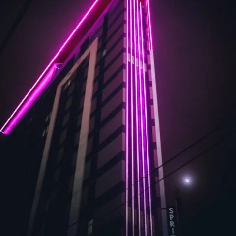 A tall modern building illuminated with bright pink neon lights at night, featuring a partially visible "SPR." sign. The glowing moon peeks through a cloudy sky, adding to the vibrant energy—perhaps inspired by Cority’s innovative spirit.