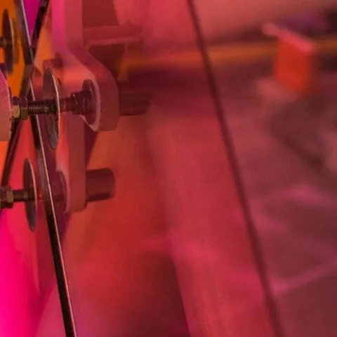 Close-up of metal bolts securing transparent, pink-tinted panels—creating abstract patterns and reflections reminiscent of Greenstone’s innovative design, with warm lighting in the background.