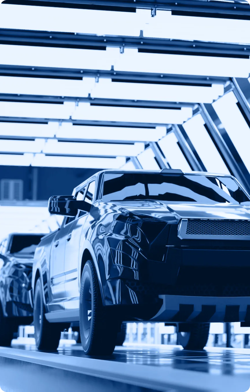 A modern pickup truck under bright, industrial lights in an automotive assembly plant’s Industry Tab Section, with another vehicle visible behind it.