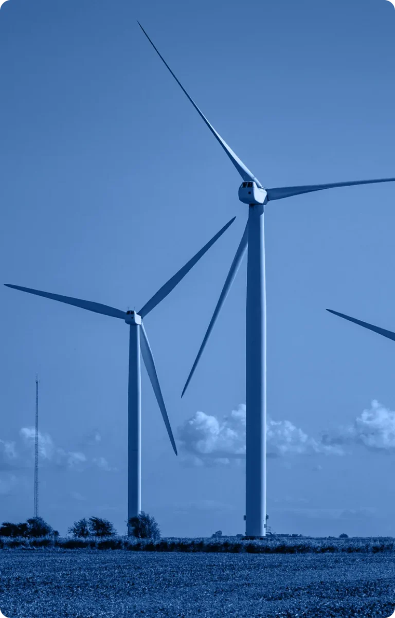 Three large wind turbines stand in an open field under a partly cloudy sky, generating renewable energy for the industry. The image features a blue color filter.