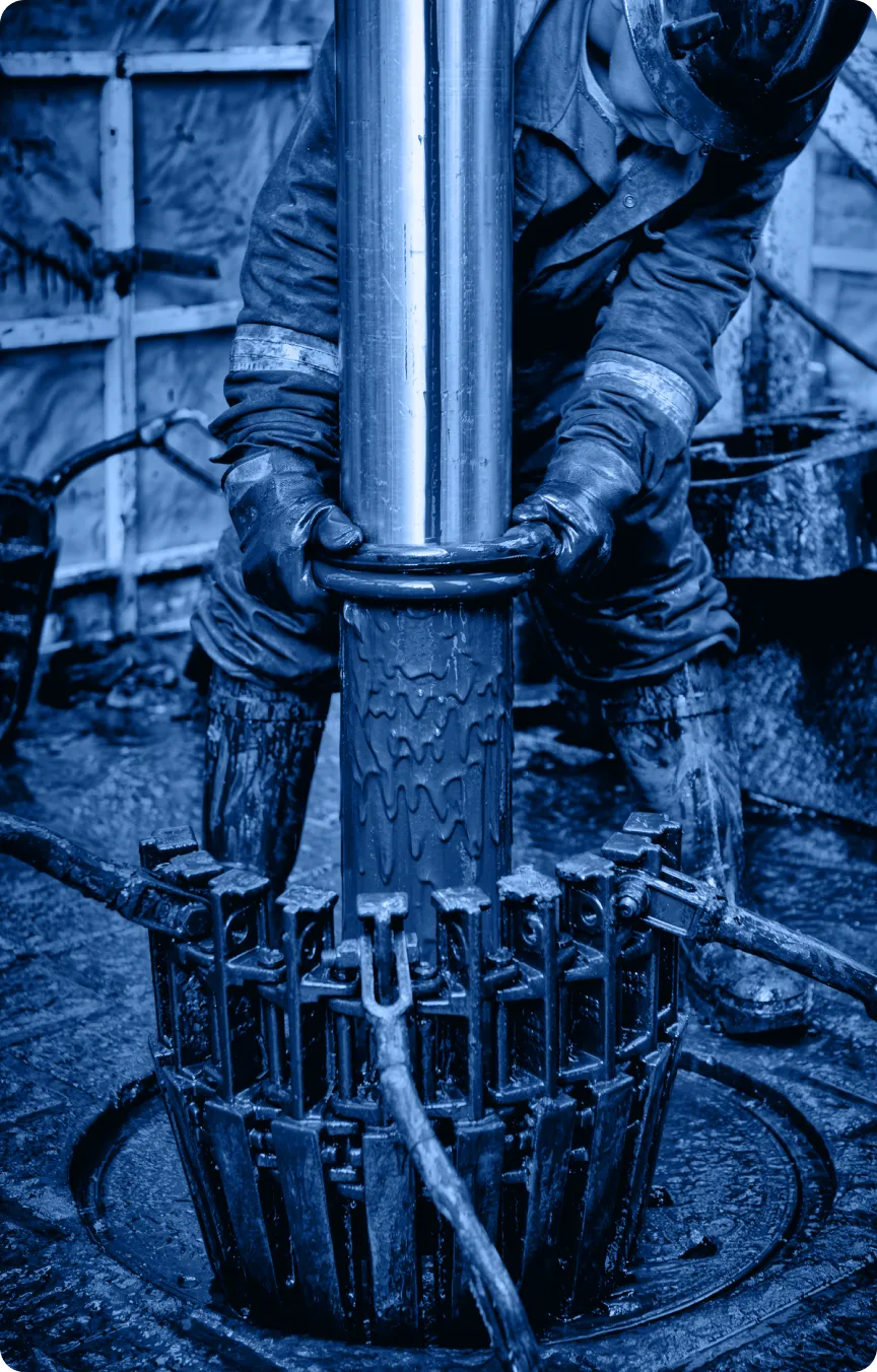 A worker in protective gear uses gloved hands to operate heavy machinery in the industry, handling a large cylindrical metal pipe—possibly part of a Tab Section—in an industrial setting with a blue tint.