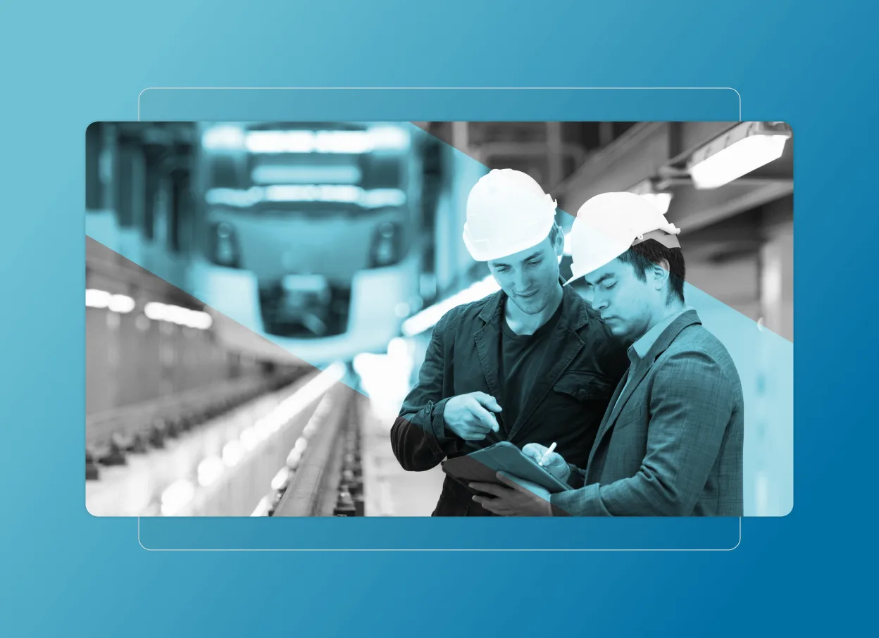 Two men wearing hard hats review documents on a clipboard in a train maintenance facility, with a blurred train in the background and a blue geometric overlay resembling a Cloud Accordion Section.