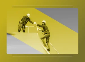 Two construction workers wearing safety gear and helmets assist each other while working on a sloped structure, highlighted by a yellow and gray-toned overlay—emphasizing teamwork and the benefits of Safety Cloud on the jobsite.