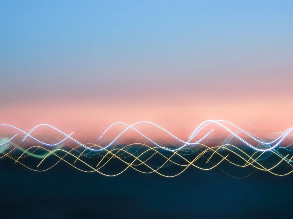 Abstract image of a sunset sky with a gradient of blue to pink and blurry, wavy lines of light in white, yellow, and blue across the bottom, resembling long-exposure photography.