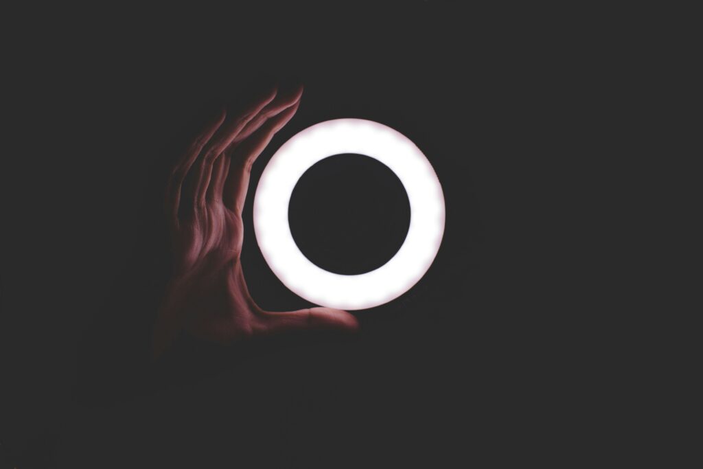 A hand holds a glowing circular ring light against a dark background, fingers gently wrapping around the bright ring—much like exploring ehs software pricing options in the spotlight.