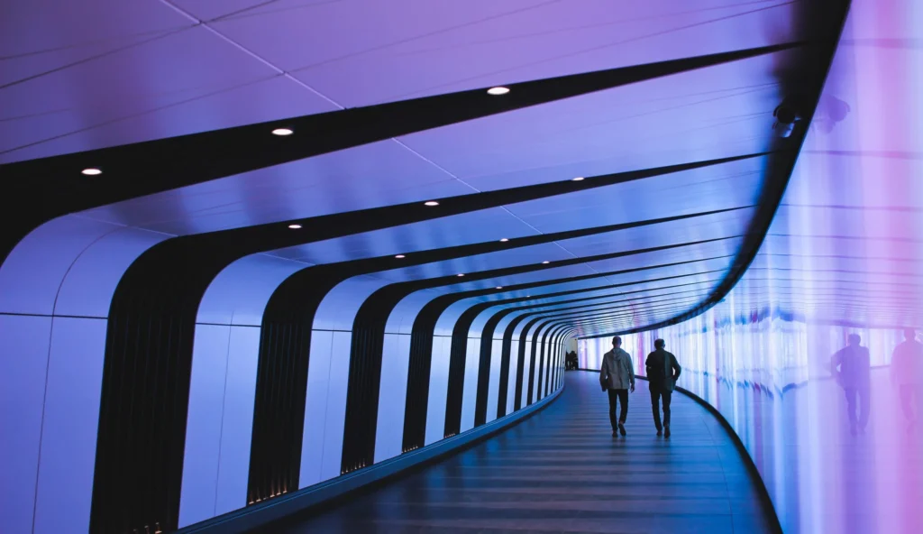 Two people walk through a futuristic, curved corridor with purple and blue lighting, glossy walls, and a striped design, reflecting a modern sci-fi atmosphere inspired by advanced Cortex AI technology.