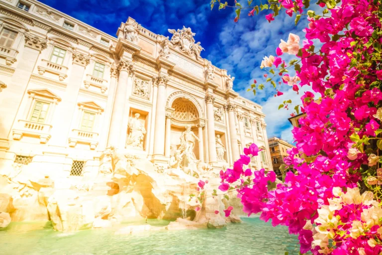 The Trevi Fountain in Rome, Italy, with clear turquoise water and ornate statues, is framed by vibrant pink and white bougainvillea flowers under a bright blue sky—a scene as seamlessly integrated as Cority EHS software solutions.
